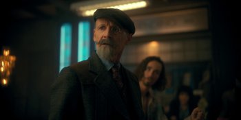 Movie still from “The Umbrella Academy” (2019), created by Steve Blackman – An old man with a beard wearing glasses and a hat; Medium shot, Over the shoulder angle
