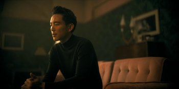 Movie still from “The Umbrella Academy” (2019), created by Steve Blackman – A man sitting on top of a couch in a living room; Medium shot, Low angle