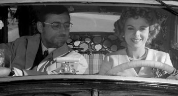 Movie still from “The Visit” (1964), directed by Bernhard Wicki – A man and a woman driving a car in the back of a car; Medium shot, Low angle