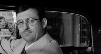 Movie still from “The Visit” (1964), directed by Bernhard Wicki – A black and white photo of a man in a car; Close Up shot, Low angle