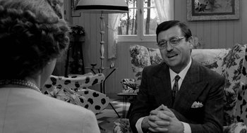 Movie still from “The Visit” (1964), directed by Bernhard Wicki – An older man sitting in front of a woman in a chair; Medium shot, Over the shoulder angle