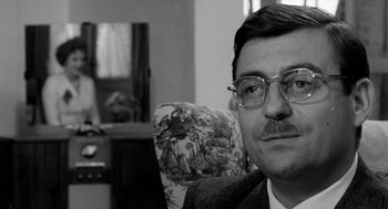 Movie still from “The Visit” (1964), directed by Bernhard Wicki – A black and white photo of a man with glasses; Close Up shot, Over the shoulder angle