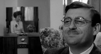 Movie still from “The Visit” (1964), directed by Bernhard Wicki – A black and white photo of a man with glasses; Close Up shot, Over the shoulder angle