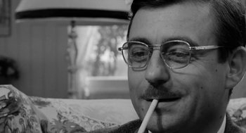 Movie still from “The Visit” (1964), directed by Bernhard Wicki – A black and white photo of a man smoking a cigarette; Close Up shot, Low angle