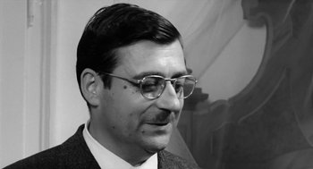 Movie still from “The Visit” (1964), directed by Bernhard Wicki – A black and white photo of a man wearing glasses; Close Up shot, Low angle