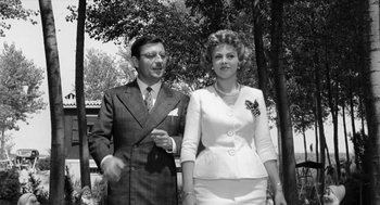 Movie still from “The Visit” (1964), directed by Bernhard Wicki – An older man standing next to an older woman; Medium shot, Low angle