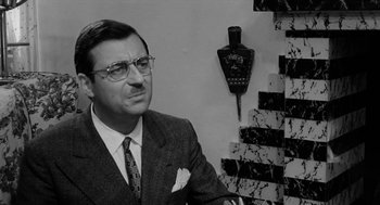 Movie still from “The Visit” (1964), directed by Bernhard Wicki – A man in a suit and tie in front of a wall; Close Up shot, High angle