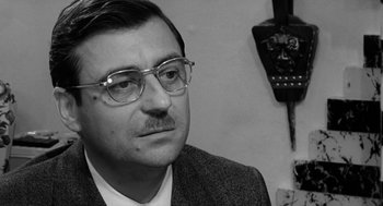 Movie still from “The Visit” (1964), directed by Bernhard Wicki – A black and white photo of a man wearing glasses; Close Up shot, Over the shoulder angle