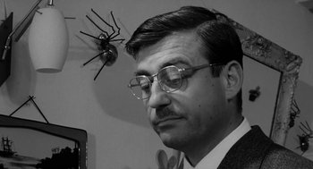 Movie still from “The Visit” (1964), directed by Bernhard Wicki – A black and white photo of a man wearing glasses; Close Up shot, Low angle