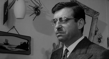 Movie still from “The Visit” (1964), directed by Bernhard Wicki – A black and white photo of a man wearing glasses; Close Up shot, Low angle