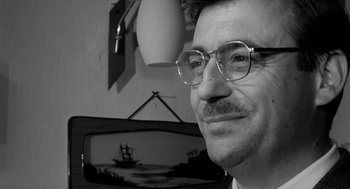 Movie still from “The Visit” (1964), directed by Bernhard Wicki – A black and white photo of a man wearing glasses; Close Up shot, Over the shoulder angle