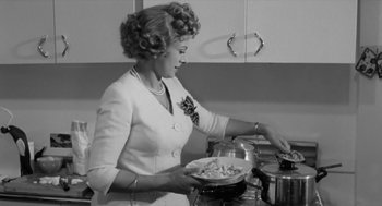 Movie still from “The Visit” (1964), directed by Bernhard Wicki – A black and white photo of a woman cooking food; Medium shot, Low angle