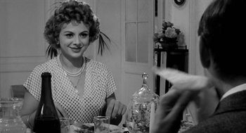 Movie still from “The Visit” (1964), directed by Bernhard Wicki – A woman sitting at a table with a glass of water; Medium shot, Over the shoulder angle