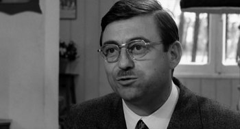 Movie still from “The Visit” (1964), directed by Bernhard Wicki – Black and white photograph of a man wearing glasses; Close Up shot, Over the shoulder angle