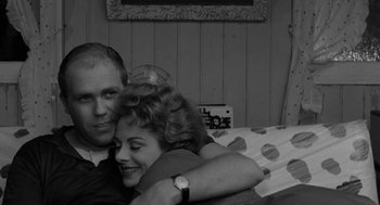 Movie still from “The Visit” (1964), directed by Bernhard Wicki – A man and a woman hugging on a couch; Medium shot, High angle
