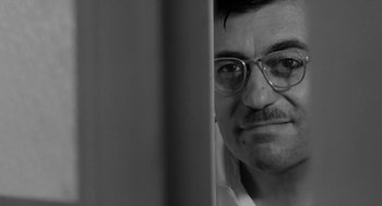 Movie still from “The Visit” (1964), directed by Bernhard Wicki – A black and white photo of a man wearing glasses; Close Up shot, Low angle