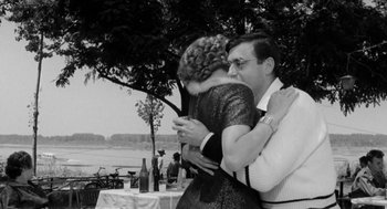 Movie still from “The Visit” (1964), directed by Bernhard Wicki – An older man and a woman hugging at an outdoor party; Medium shot, Over the shoulder angle