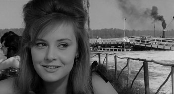 Movie still from “The Visit” (1964), directed by Bernhard Wicki – A young woman is standing in front of a body of water; Close Up shot, Over the shoulder angle