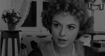 Movie still from “The Visit” (1964), directed by Bernhard Wicki – A black and white photo of a woman wearing pearls; Close Up shot, Over the shoulder angle