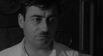 Movie still from “The Visit” (1964), directed by Bernhard Wicki – Black and white photograph of a man looking at the camera; Close Up shot, Low angle