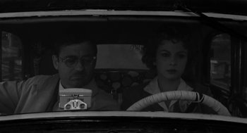 Movie still from “The Visit” (1964), directed by Bernhard Wicki – A man and a woman sitting in the back seat of a car; Close Up shot, Low angle