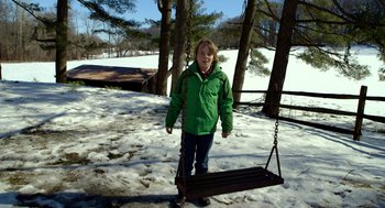 Movie still from “The Visit” (2015), directed by M. Night Shyamalan – A boy in a green jacket is standing on a swing; Wide shot, High angle