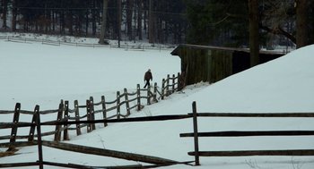 Movie still from “The Visit” (2015), directed by M. Night Shyamalan – A person walking in the snow near a wooden fence; Extreme Wide shot, High angle