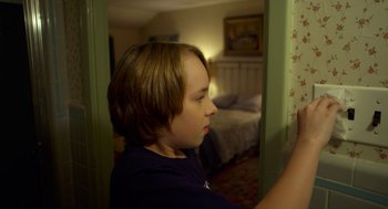 Movie still from “The Visit” (2015), directed by M. Night Shyamalan – A young boy looking out of a bedroom window; Close Up shot, Over the shoulder angle