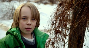 Movie still from “The Visit” (2015), directed by M. Night Shyamalan – A young boy in a green jacket standing next to a tree; Close Up shot, Over the shoulder angle