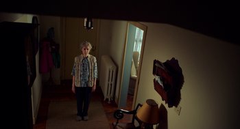 Movie still from “The Visit” (2015), directed by M. Night Shyamalan – An older woman standing in front of a mirror in a living room; Wide shot, Low angle