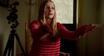 Movie still from “The Visit” (2015), directed by M. Night Shyamalan – A young girl in a red striped shirt is playing a video game; Medium shot, Over the shoulder angle