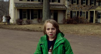 Movie still from “The Visit” (2015), directed by M. Night Shyamalan – A boy in a green jacket standing in front of a house; Medium shot, Over the shoulder angle