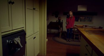 Movie still from “The Visit” (2015), directed by M. Night Shyamalan – A woman standing in a living room holding a cell phone; Wide shot, High angle