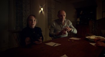Movie still from “The Visit” (2015), directed by M. Night Shyamalan – Two people sitting at a wooden table in a room; Medium shot, Over the shoulder angle