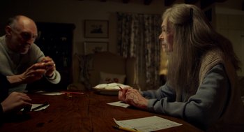 Movie still from “The Visit” (2015), directed by M. Night Shyamalan – An older woman sitting at a wooden table writing on paper; Medium shot, Over the shoulder angle
