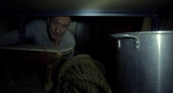 Movie still from “The Visit” (2015), directed by M. Night Shyamalan – A man peeking out from under a table with ropes; Medium shot, High angle