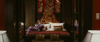 Movie still from “The Walker” (2007), directed by Paul Schrader – A person laying on top of a bed in front of a painting; Wide shot, Overhead angle