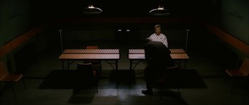 Movie still from “The Walker” (2007), directed by Paul Schrader – A man standing in front of two tables in a dark room; Wide shot, Over the shoulder angle