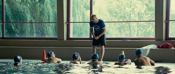 Movie still from “The Wave” (2008), directed by Dennis Gansel – A group of people in a pool with a man in a blue t - shirt; Wide shot, Over the shoulder angle