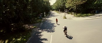 Movie still from “The Wave” (2008), directed by Dennis Gansel – Two bicyclists riding down the street on a sunny day; Extreme Wide shot, High angle