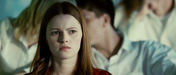 Movie still from “The Wave” (2008), directed by Dennis Gansel – A young woman with red hair looking at the camera with a man in the background; Close Up shot, Over the shoulder angle