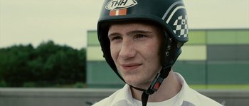 Movie still from “The Wave” (2008), directed by Dennis Gansel – A young man wearing a motorcycle helmet and smiling; Close Up shot, Low angle