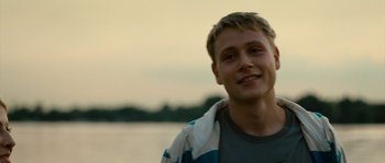 Movie still from “The Wave” (2008), directed by Dennis Gansel – A young man smiling for the camera near a body of water; Close Up shot, Over the shoulder angle