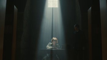 Movie still from “Anne with an E” (2017), created by Moira Walley-Beckett – A woman sitting at a table in a room with a light shining through the window; Wide shot, Low angle