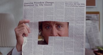 Movie still from “The Woman in Red” (1984), directed by Gene Wilder – A person is looking through a hole in a newspaper; Extreme Close Up shot, Over the shoulder angle