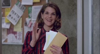 Movie still from “The Woman in Red” (1984), directed by Gene Wilder – A woman in a red and black striped shirt holding a piece of paper; Medium shot, Over the shoulder angle