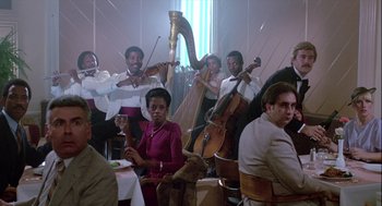 Movie still from “The Woman in Red” (1984), directed by Gene Wilder – A group of people that are sitting in a room; Wide shot, Low angle
