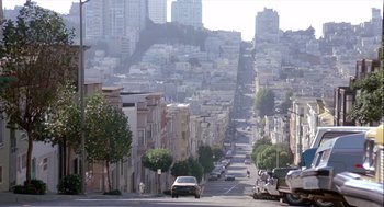 Movie still from “The Woman in Red” (1984), directed by Gene Wilder – A view of a street with cars driving down it; Extreme Wide shot, High angle