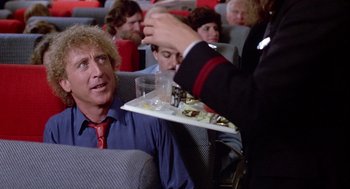 Movie still from “The Woman in Red” (1984), directed by Gene Wilder – A person serving a tray of food to a man in the audience; Medium shot, Over the shoulder angle