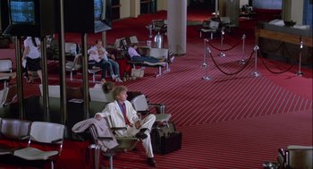 Movie still from “The Woman in Red” (1984), directed by Gene Wilder – A man sitting on a chair in an airport terminal; Wide shot, High angle